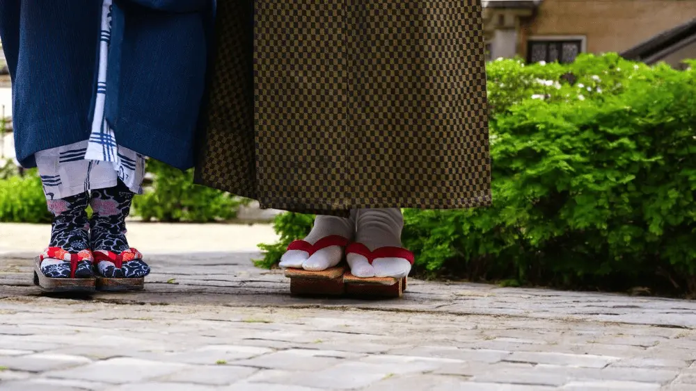 Zwei Personen in traditioneller japanischer Kleidung mit Tabi-Socken und Geta-Holzsandalen auf Kopfsteinpflaster.