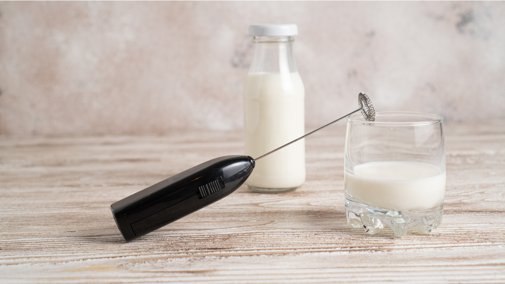 Milchaufschäumer, ein Milchglas und eine Milchflasche stehen auf einem Tisch